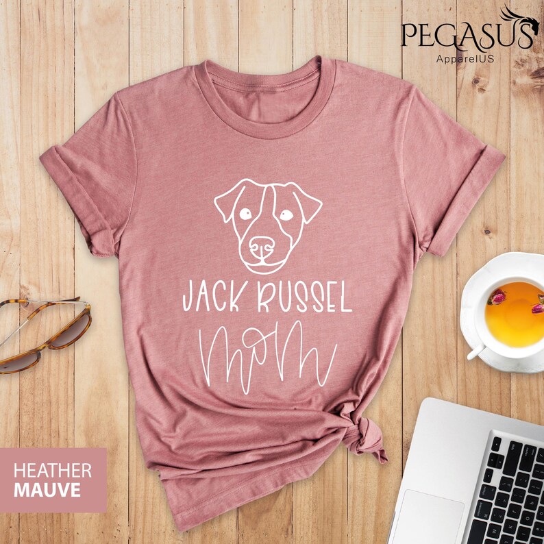 May include: Heather mauve t-shirt with a white graphic of a Jack Russell Terrier dog face and the words "JACK RUSSEL MOM" in a script font. The shirt is folded at the bottom. The brand name "Pegasus Apparel US" is in the top right corner.