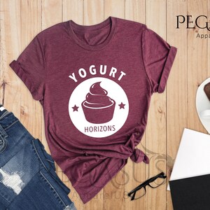 May include: A maroon t-shirt with a white graphic of a yogurt cup and the text "Yogurt Horizons".
