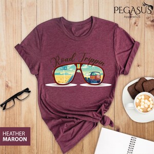 Peut inclure: T-shirt en marron chin&eacute; avec un motif de lunettes de soleil refl&eacute;tant une sc&egrave;ne de road trip. Le texte "Road Trippin'" est au-dessus des lunettes de soleil.