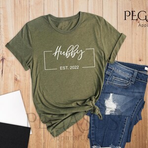 May include: A green heather olive t-shirt with the text "Hubby Est. 2022" in a white box.