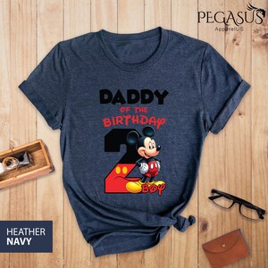 May include: Heather navy t-shirt with the text "DADDY of the BIRTHDAY 2 BOY" and a graphic of Mickey Mouse. The number 2 is red and black, with Mickey Mouse standing on the number 2. The shirt is from Pegasus ApparelUS.