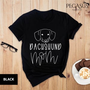 May include: Black t-shirt with a white outline of a dachshund and the text "Dachshund Mom" in white.