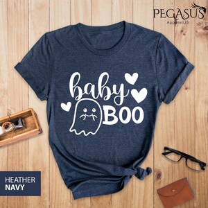 May include: Heather navy blue t-shirt with the words "baby BOO" in white script and a ghost graphic. The shirt has a crew neck and short sleeves. The text "HEATHER NAVY" is in a navy blue rectangle in the bottom left corner.