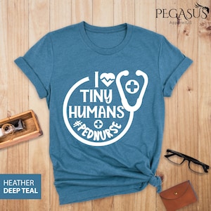 Op de afbeelding: Een tealblauw t-shirt met een wit grafisch ontwerp met de tekst "Ik hou van kleine mensen #pednurse" met een stethoscoop en een hartgrafiek.