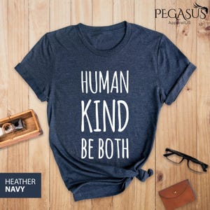 May include: A heather navy blue t-shirt with the text "HUMAN KIND BE BOTH" printed in white.
