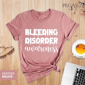 May include: A heather mauve t-shirt with the text "Bleeding Disorder awareness" in white dripping letters.
