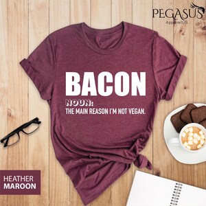 May include: A maroon t-shirt with the text "BACON NOUN: THE MAIN REASON I'M NOT VEGAN." printed in white.