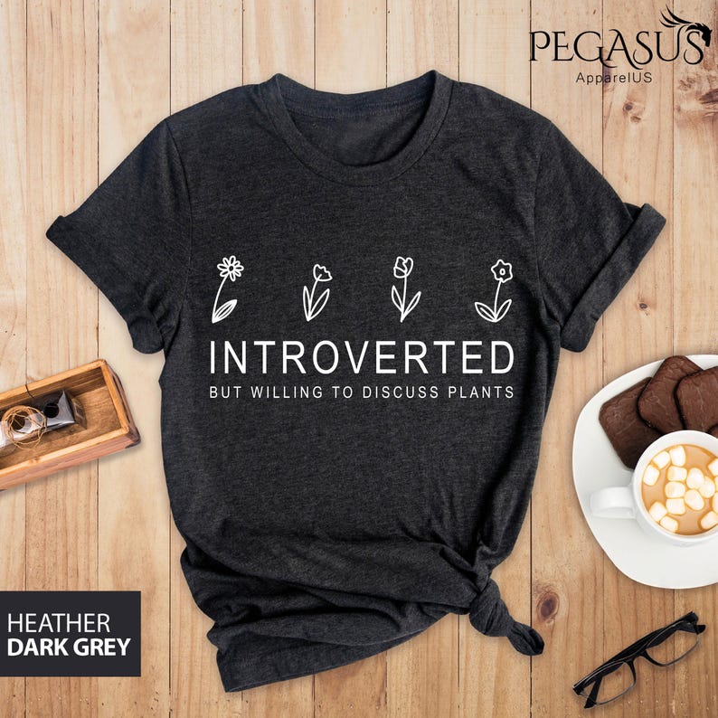 May include: Dark heather grey t-shirt with a white graphic of flowers and the text "Introverted but willing to discuss plants".