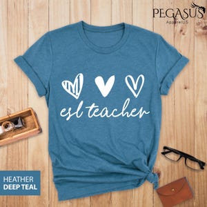 May include: A teal blue t-shirt with a white graphic of three hearts and the text "esl teacher".