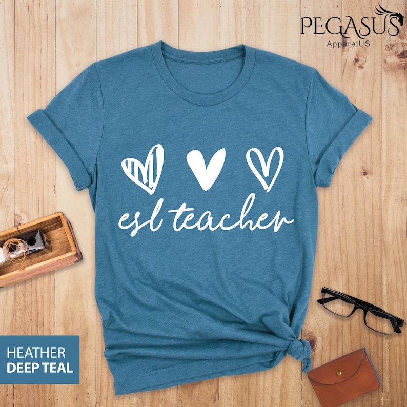 May include: A teal blue t-shirt with a white graphic of three hearts and the text "esl teacher".