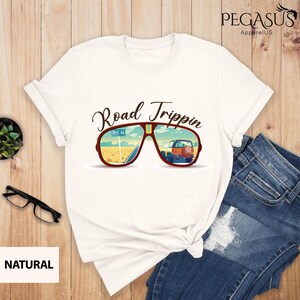 Peut inclure: T-shirt blanc avec un graphique de lunettes de soleil refl&eacute;tant une route d&eacute;sertique avec une voiture roulant sur la Route 66. Le texte "Road Trippin'" est au-dessus des lunettes de soleil.