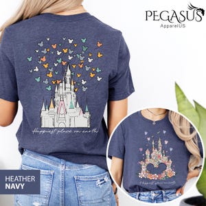Op de afbeelding: Een heideblauwe t-shirt met een afbeelding van Assepoester's kasteel en Mickey Mouse ballonnen. De tekst "Happiest place on earth" is onder het kasteel gedrukt.