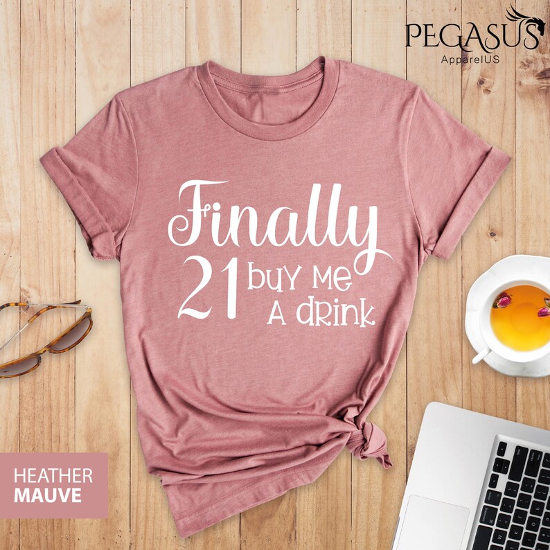 May include: A heather mauve t-shirt with the text "Finally 21 buy me a drink" printed in white.