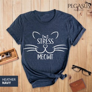 Op de afbeelding: Heather navyblauw t-shirt met een witte kattenkop-afbeelding en de tekst "Don't Stress Meowt".