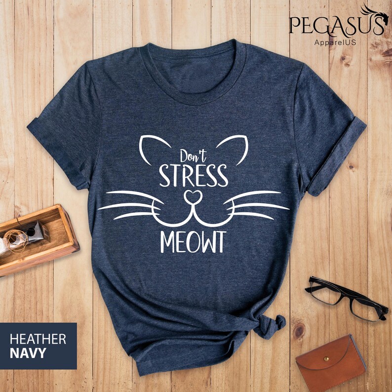 Op de afbeelding: Heather navyblauw t-shirt met een witte kattenkop-afbeelding en de tekst "Don't Stress Meowt".