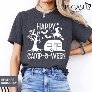 May include: Dark grey t-shirt featuring the white text "HAPPY CAMP-O-WEEN" with a tree, bats, a witch, and a caravan graphic. The shirt is a short-sleeved crew neck, perfect for Halloween camping.