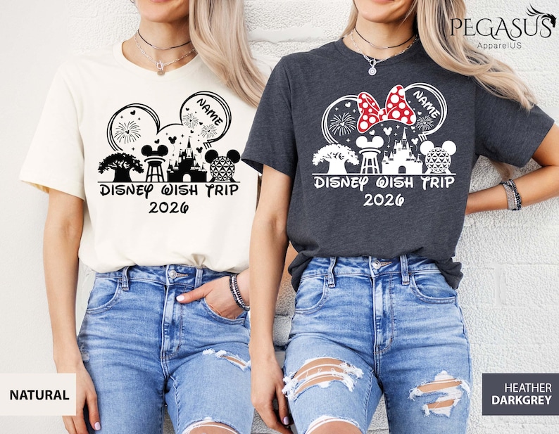 May include: Two t-shirts, one natural and one heather dark grey, featuring a Disney-themed graphic. The design includes Mickey Mouse ears, a castle, fireworks, and the text "Disney Wish Trip 2026". The natural shirt has a black graphic, while the dark grey shirt has a white and red graphic.