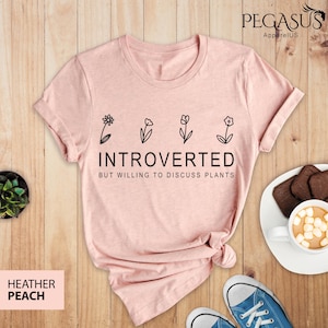 May include: A heather peach t-shirt with a graphic of five flowers and the text "Introverted but willing to discuss plants".