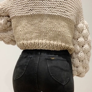 back of bubble sleeve chunky knitted cardigan. the body is made up of stockinette stitch and knit stitch. the sleeves are made from bubble stitch and 1x1 rib stitch. the cardigan is a cropped oversized relaxed fit.