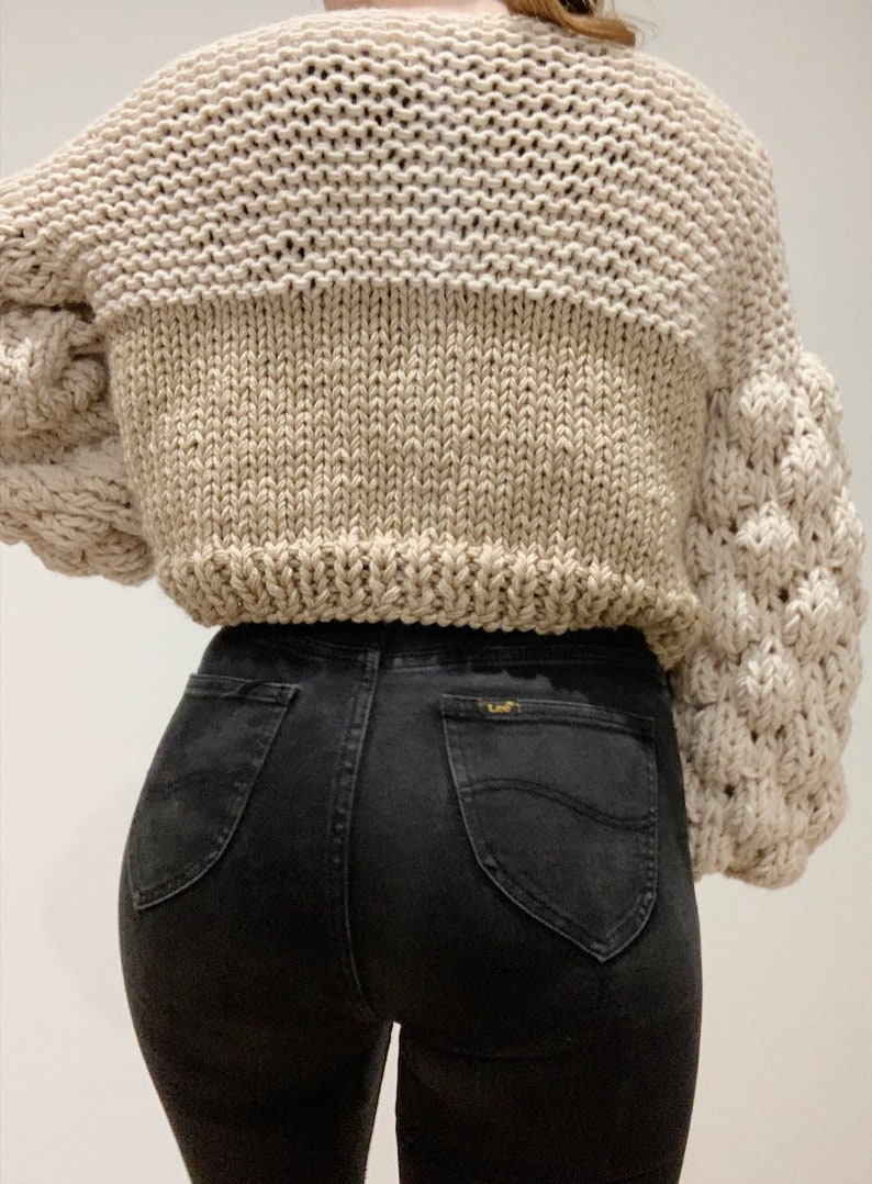 back of bubble sleeve chunky knitted cardigan. the body is made up of stockinette stitch and knit stitch. the sleeves are made from bubble stitch and 1x1 rib stitch. the cardigan is a cropped oversized relaxed fit.