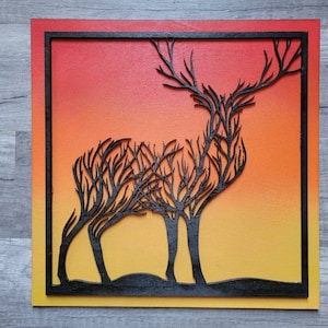 May include: A black silhouette of a deer with antlers, made of branches, is set against a gradient background of red, orange, and yellow. The deer is framed by a black square.