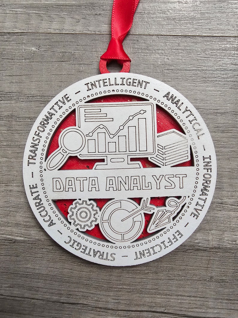 May include: A round white wooden ornament with a red backing and a red ribbon hanger. The center features a computer monitor with a line graph, a magnifying glass, a stack of papers, a gear, a pie chart, and the text DATA ANALYST.