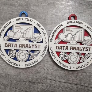 May include: Two circular wooden ornaments featuring the text DATA ANALYST. One has a blue backing and the other a red backing. The white front layer displays icons of a computer monitor with a line graph, a magnifying glass, a stack of papers, a gear, and a target with an arrow. The border includes the words INTELLIGENT, ANALYTICAL, INFORMATIVE, EFFICIENT, STRATEGIC, ACCURATE, and TRANSFORMATIVE.