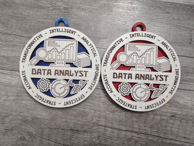 May include: Two circular wooden ornaments featuring the text DATA ANALYST. One has a blue backing and the other a red backing. The white front layer displays icons of a computer monitor with a line graph, a magnifying glass, a stack of papers, a gear, and a target with an arrow. The border includes the words INTELLIGENT, ANALYTICAL, INFORMATIVE, EFFICIENT, STRATEGIC, ACCURATE, and TRANSFORMATIVE.