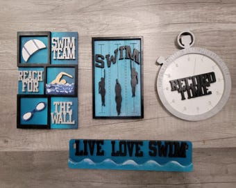 May include: Wooden swimming-themed wall art. Includes a stopwatch with "Record Time" text, a sign with "Live Love Swim", and framed art pieces with swimming-related imagery and text like "Swim Team" and "Reach for the Wall".
