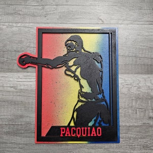 May include: Black silhouette of a boxer throwing a punch, with a red, yellow, and blue gradient background. The name "PACQUIAO" is written in red letters at the bottom of the image.
