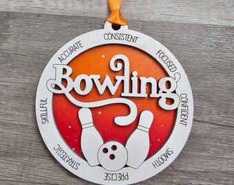 May include: White wooden round ornament with the word "Bowling" in a stylized font. The ornament has a red and orange gradient background with white bowling pins and a bowling ball. The words "Accurate, Consistent, Focused, Confident, Skillful, Strategic, Precise, Smooth" are written around the edge of the ornament.