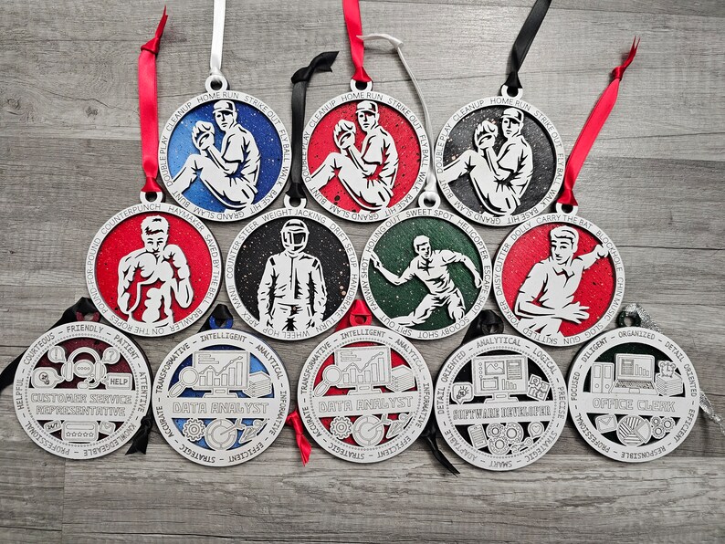 May include: A collection of eleven circular wooden ornaments featuring various professions and sports themes. Each ornament displays a central white graphic, a colored background, and a border with engraved text, suspended by colorful ribbons.