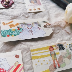 May include: A set of four Christmas-themed paper tags with various designs. One tag features a white background with three girls in white dresses and red ribbons, with the text "Joyeux Noel". Another tag has a yellow background with a girl in a red and white dress, with the text "BO" in black letters. The other two tags have a white background with various patterns and designs.