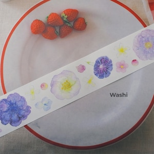 May include: A white washi tape with watercolor floral designs in shades of purple, yellow, and pink. The tape is on a white plate with red trim and a few red strawberries.