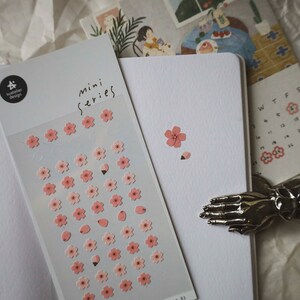 May include: A sheet of pink and white flower stickers with the text "mini series" on the top. The stickers are on a white background.