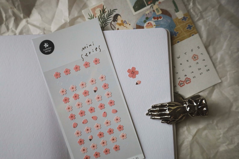 May include: A sheet of pink and white flower stickers with the text "mini series" on the top. The stickers are on a white background.