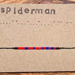 May include: A beaded bracelet with a color pattern of red, blue, and black beads on a black string. The bracelet is displayed on a brown card with the word "spiderman" printed at the top.