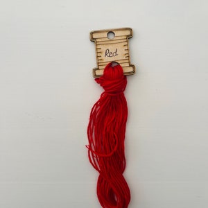 May include: A wooden spool labelled "Red" with a length of red embroidery floss attached.