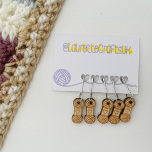 May include: A set of six wooden yarn stitch markers with a heart and yarn spool design. The markers are attached to silver rings and are displayed on a white card with the text "@laurettecraftsuk".