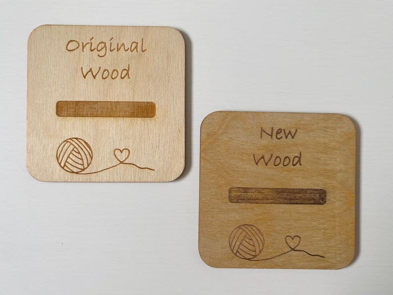 May include: Two wooden signs with the text "Original Wood" and "New Wood" engraved on them. Each sign has a slot for a yarn ball and a small heart design.