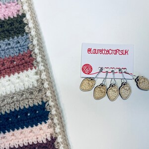 May include: A set of six strawberry-shaped stitch markers on a white card with the text "@laurettecraftsuk". The markers are made of wood and have a silver metal loop.