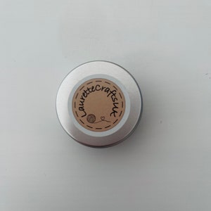 May include: A silver metal tin with a brown label that says "Laurette Crafts" with a small yarn ball and heart icon.