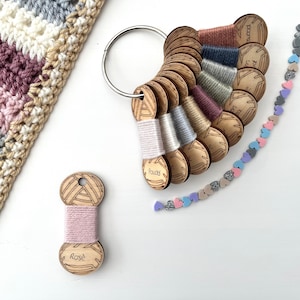 May include: A set of wooden yarn holders with different coloured yarn samples. The yarn holders are arranged in a circle and labelled with the names of the colours. There is also a single yarn holder with a pink yarn sample labelled "Rose".
