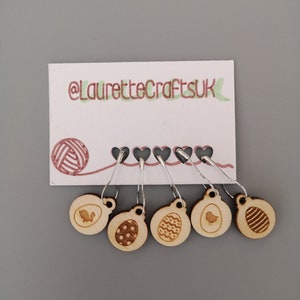 May include: Five wooden stitch markers with silver clasps, each with an Easter design. The markers are attached to a white card with the text "@LauretteCraftsUK" and a yarn ball illustration. Ideal for knitting and crochet.