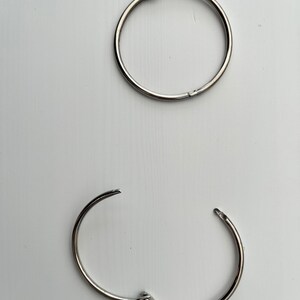 May include: Two silver binder rings, one closed and one open, on a white background.