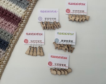 May include: Five sets of wooden stitch markers with different animal designs. Each set includes five markers with a heart-shaped loop and a silver wire. The designs include llamas, bunnies, sheep, goats, and deer. The cards each have the text "elaurettecraftsUK".