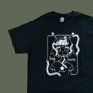 May include: Black t-shirt with a white graphic design. The design features a cartoon illustration of a person with a bug-like appearance, a brain, and the words "bug brain" and "gross". The shirt is made of a soft material.