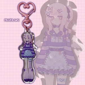 May include: A pink heart-shaped clasp keychain with a charm featuring a purple and blue anime-style character. The character has long hair and is wearing a dress. The word "mizuki" is printed on the left side.