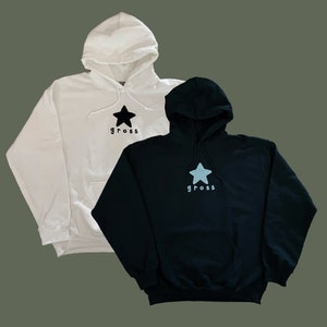 May include: Two hooded sweatshirts, one white with a black star and the word "gross" printed on it, and one black with a light blue star and the word "gross" printed on it.
