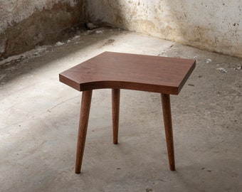 May include: A small, wooden side table with a curved top and three legs. The table is made of dark brown wood and has a natural finish.